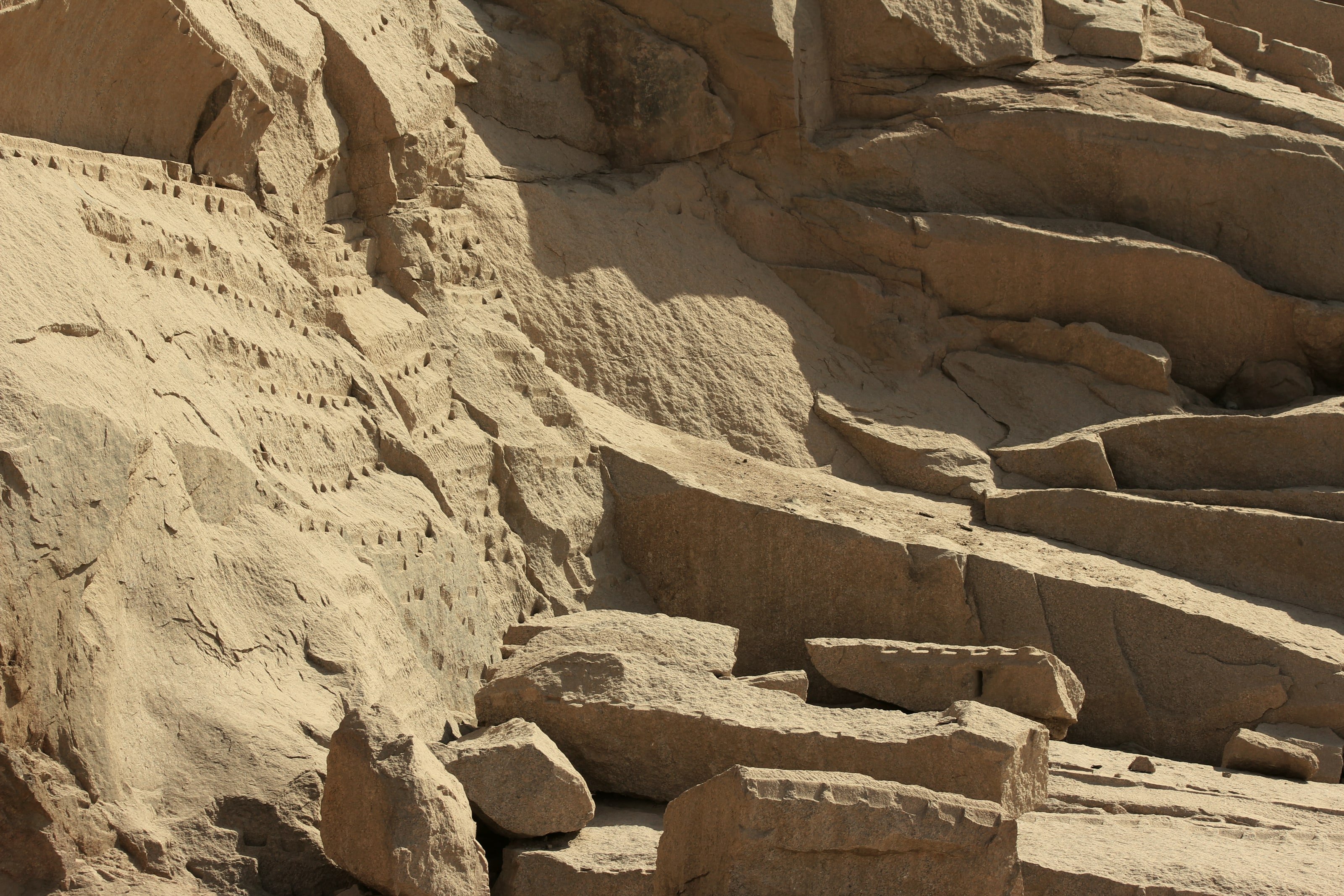 واجهة محجر جرانيت في أسوان بآثار الأدوات وكتل مقطوعة في ضوء جانبي.